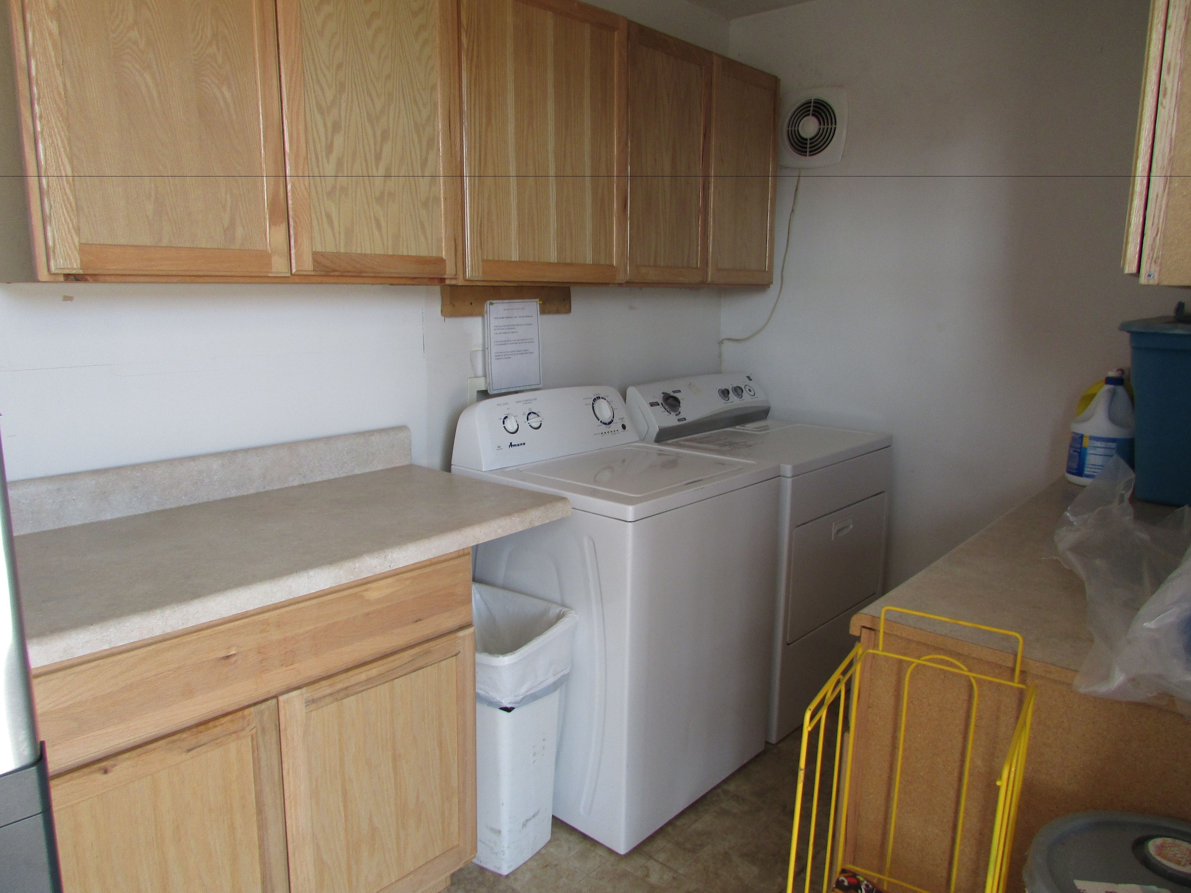 A laundry area with wooden cabinets, a washing machine, a dryer, and a small trash bin.