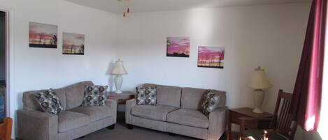 A living room with two grey sofas, a ceiling fan, and three wall-mounted paintings.