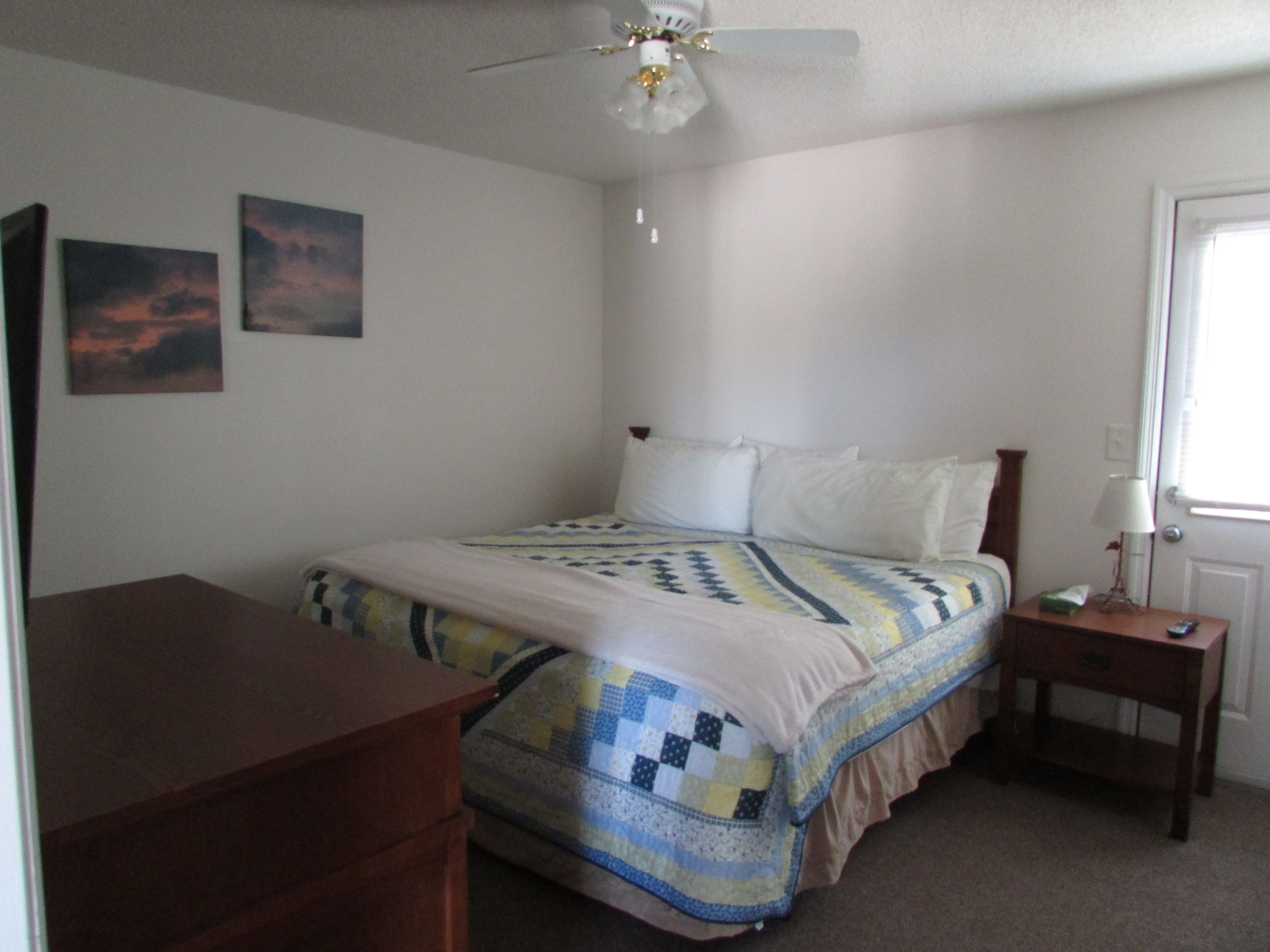 A bedroom with a bed, a nightstand, a dresser, and two wall-mounted paintings.