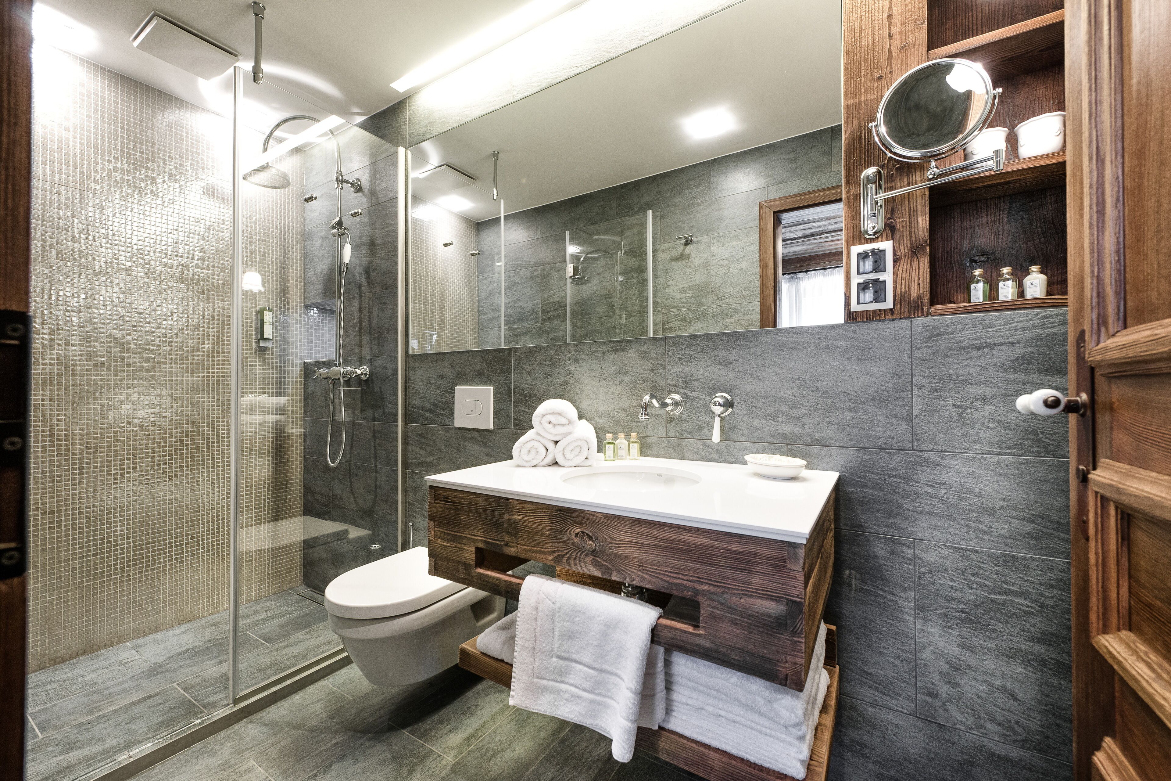 Un baño moderno con ducha de vidrio, tocador de madera y un espejo grande.