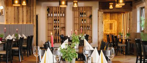 A restaurant with wooden walls, multiple tables set with white napkins, wine glasses, and candles.