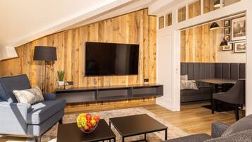 Een moderne woonkamer met een houten accentmuur, een flatscreen-televisie, een bank, een salontafel met fruit en een eethoek.
