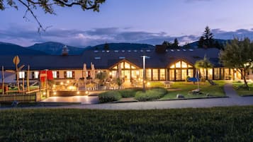 A hotel with a traditional European architectural style, featuring a courtyard with outdoor seating and a view of mountains in the background.