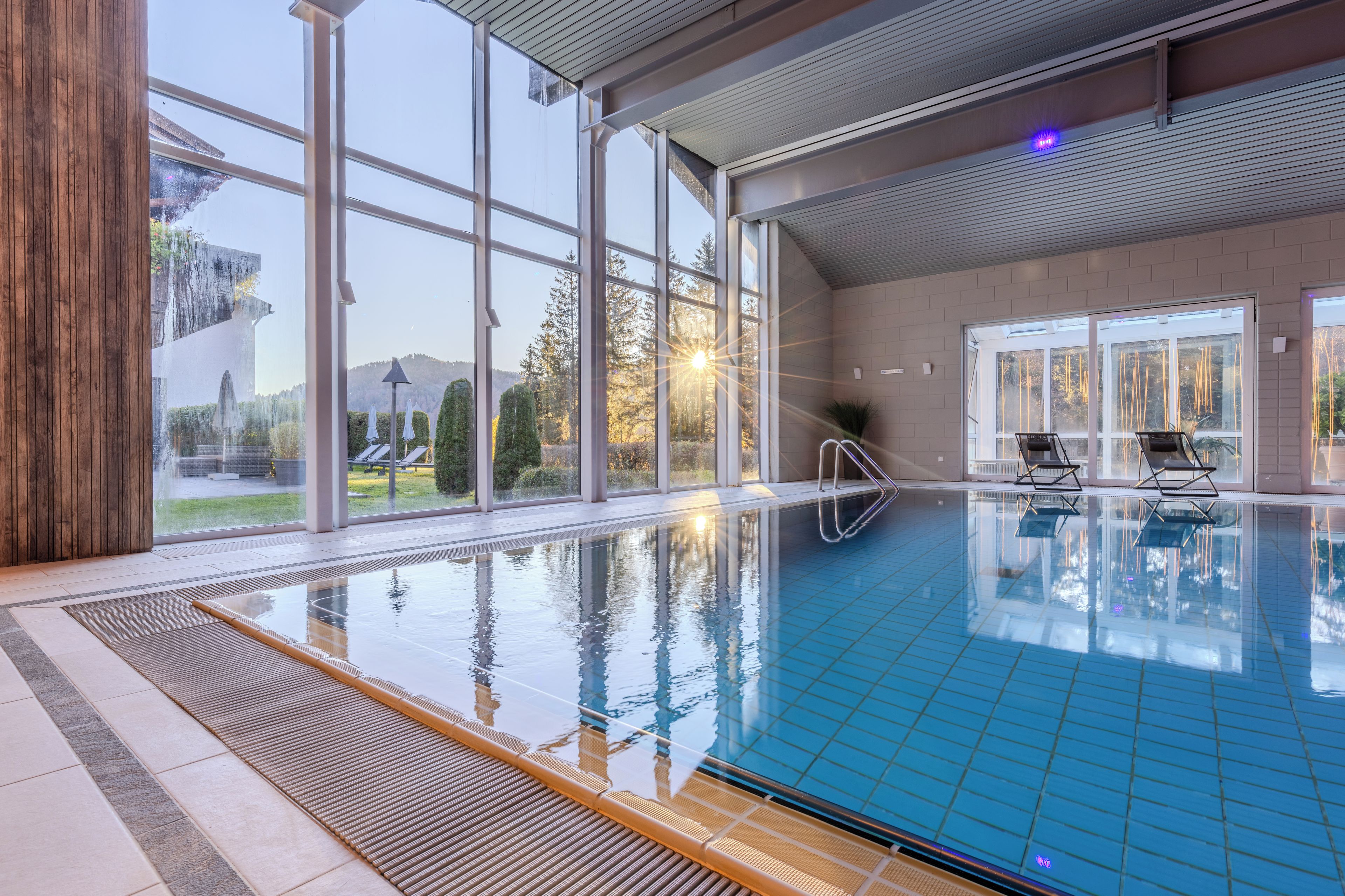 An indoor swimming pool with clear glass walls, a tiled floor, and a view of the outdoors.