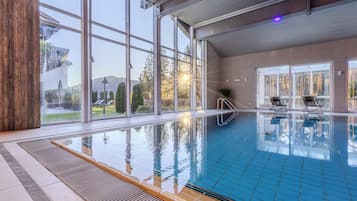 An indoor swimming pool with clear glass walls, a tiled floor, and a view of the outdoors.