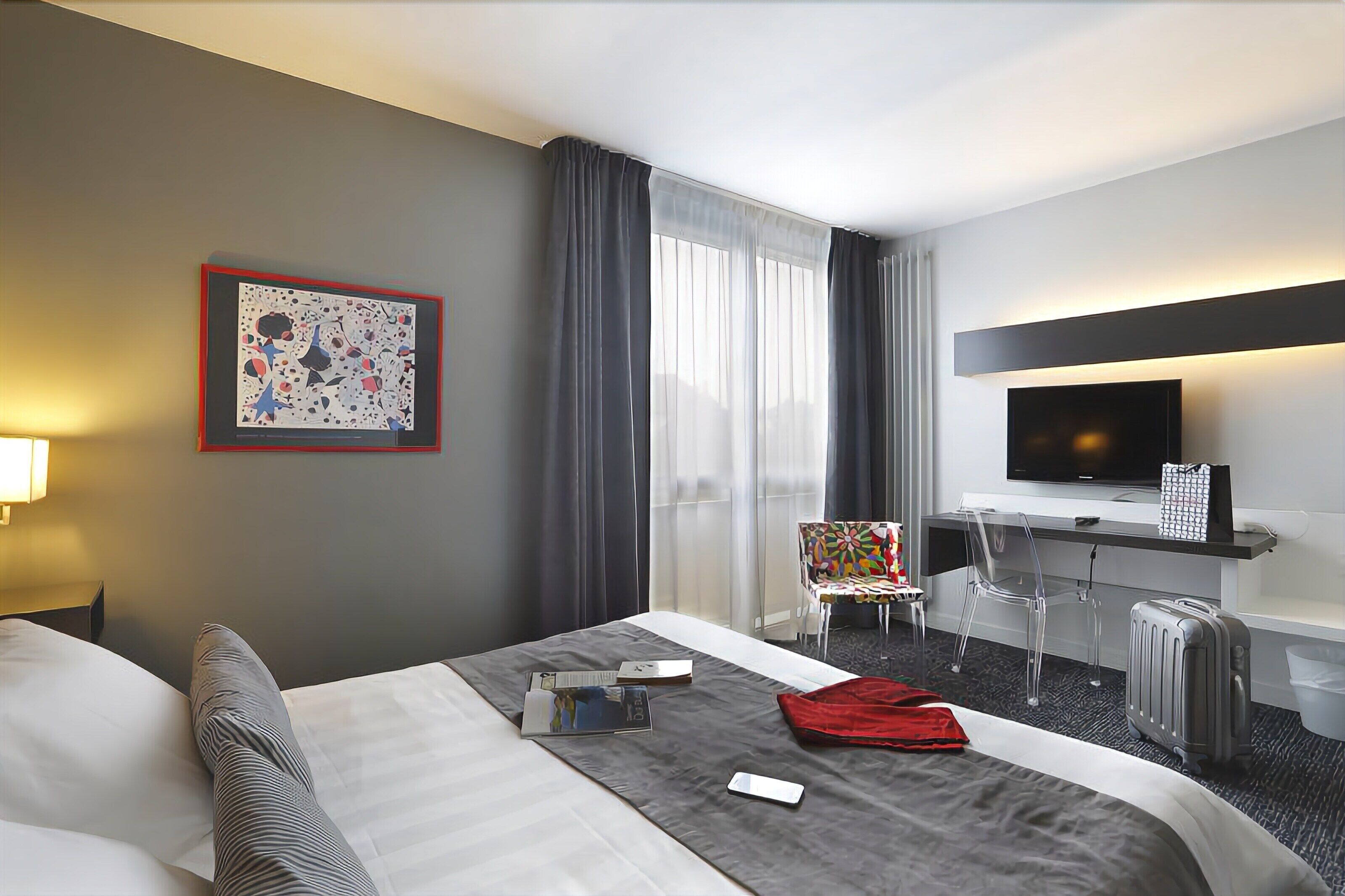 Hotellihuone, jossa on sänky, työpöytä, tuoli, televisio ja matkalaukku.