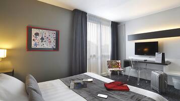 Una habitación de hotel con cama, escritorio, silla, televisor y maleta.