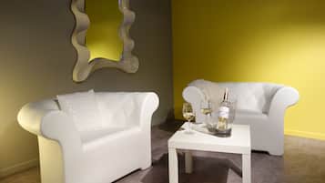 Una habitación moderna con dos sofás blancos, una mesa blanca con vasos y una botella, y un espejo decorativo en la pared.