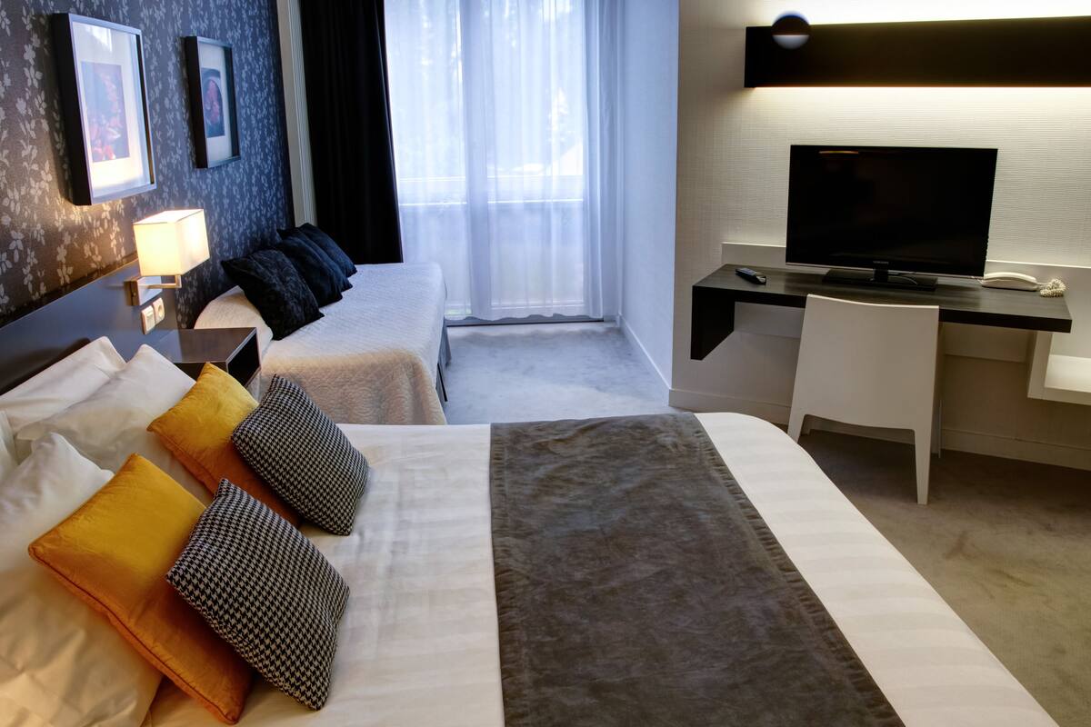 Une chambre d’hôtel avec un grand lit, un bureau avec une télévision et une fenêtre avec des rideaux légers.