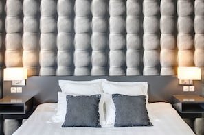 Contemporary hotel room with a tufted headboard, white linens, and bedside tables with lamps.