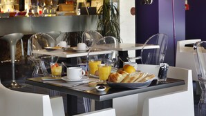 A breakfast setting with a table set for two, including croissants, orange juice, and a coffee cup.