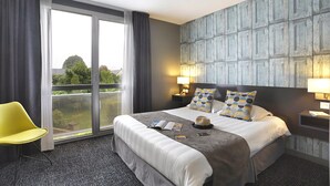A hotel room with a large bed, a yellow chair, a view through a sliding door, and a textured wall.