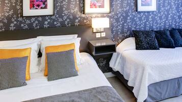A hotel room with two beds, a nightstand with a lamp, and floral wallpaper.