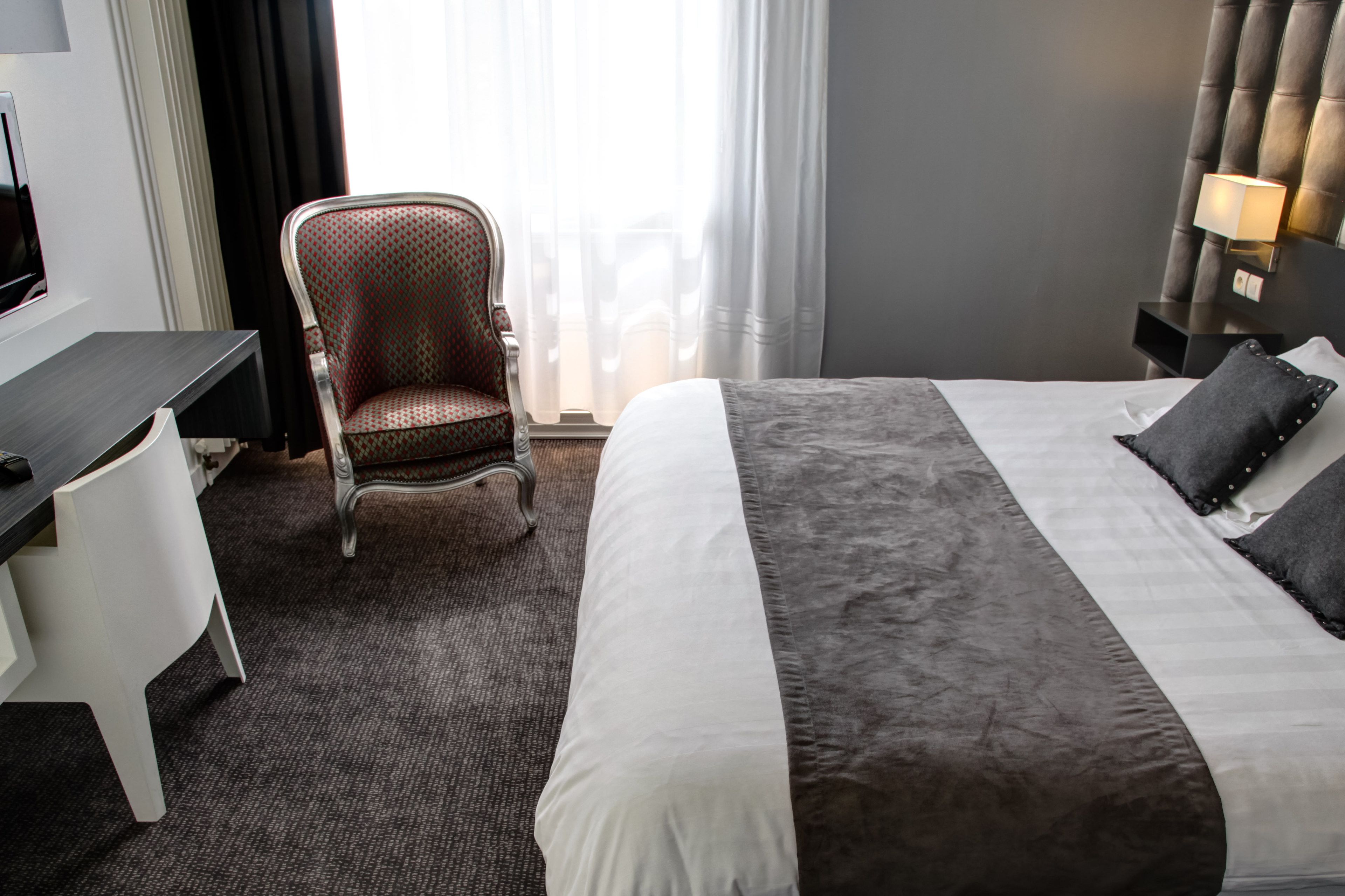 A hotel room with a bed, a desk, a chair, and a TV.