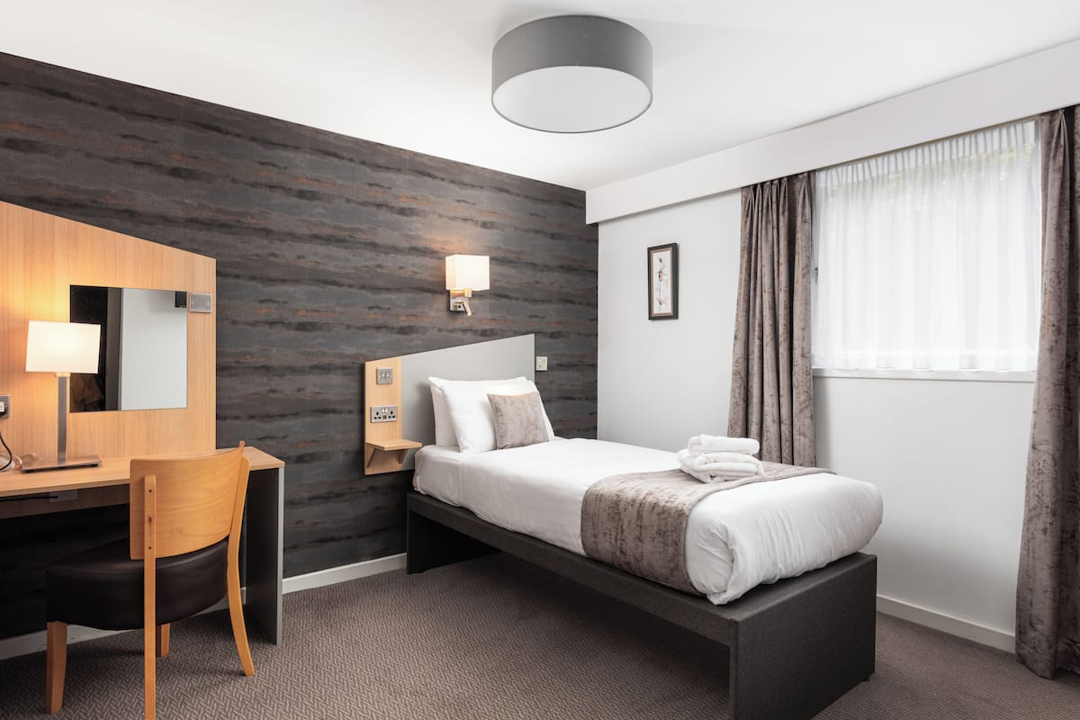 A modern hotel room with a bed, desk, chair, and a large window with curtains.