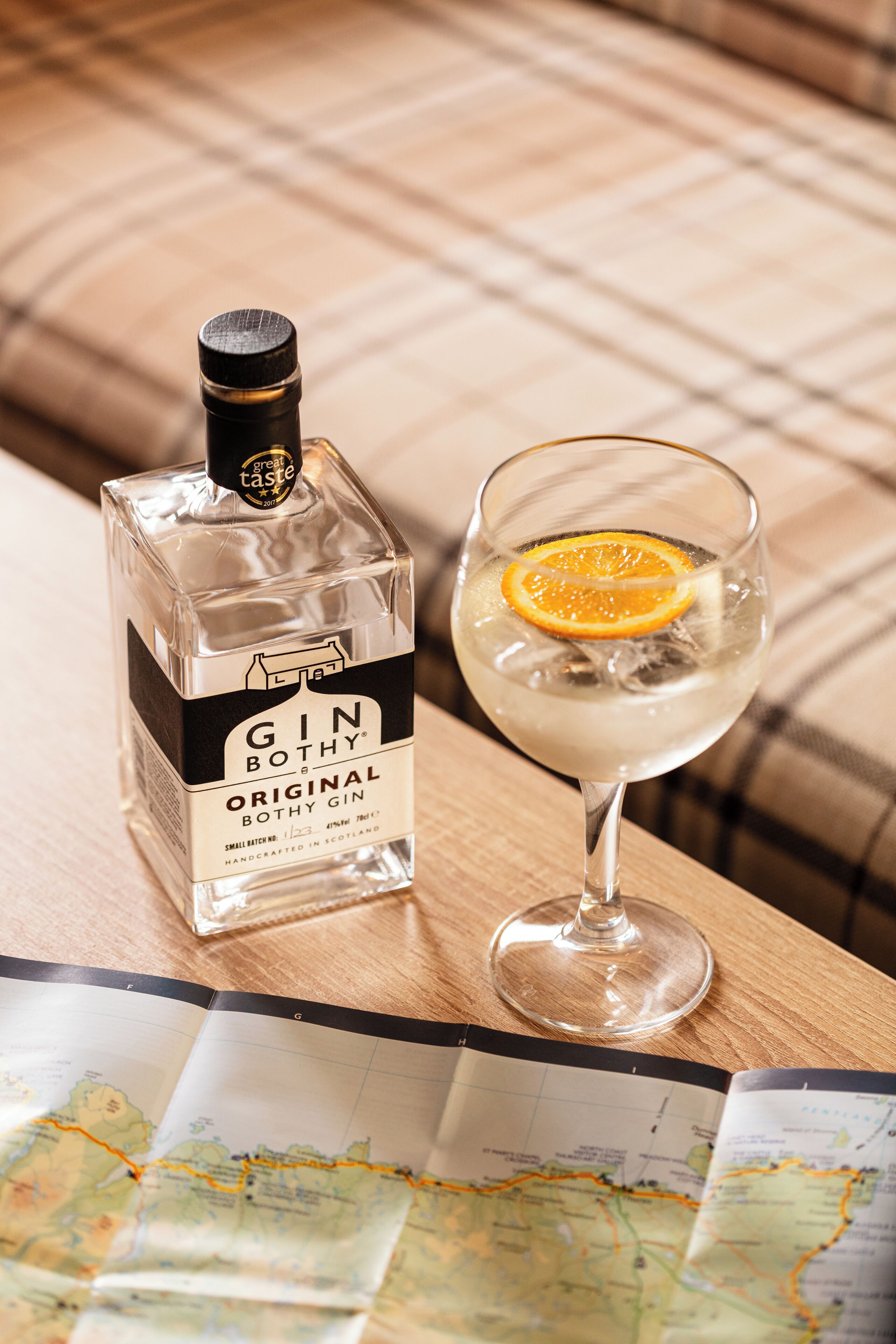 Une bouteille de gin et un verre de gin, avec une tranche d’orange, sur une table en bois, à côté d’une carte.