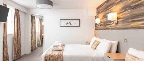 Een hotelkamer met een groot bed, een kleiner bed, een bureau en een televisie aan de muur.