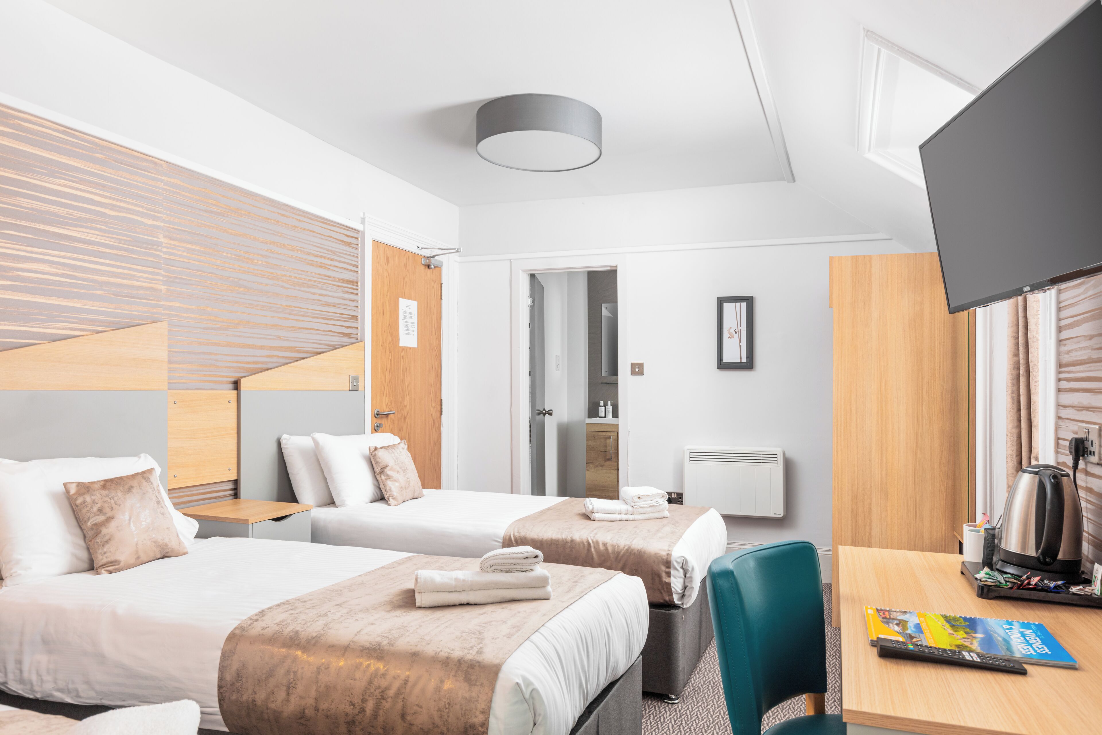 Una habitación de hotel con dos camas, un escritorio con silla, televisor y cafetera.