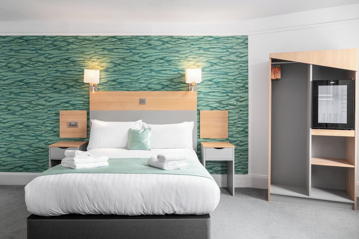 A hotel room with a bed, two bedside lamps, a wardrobe, and a built-in TV.