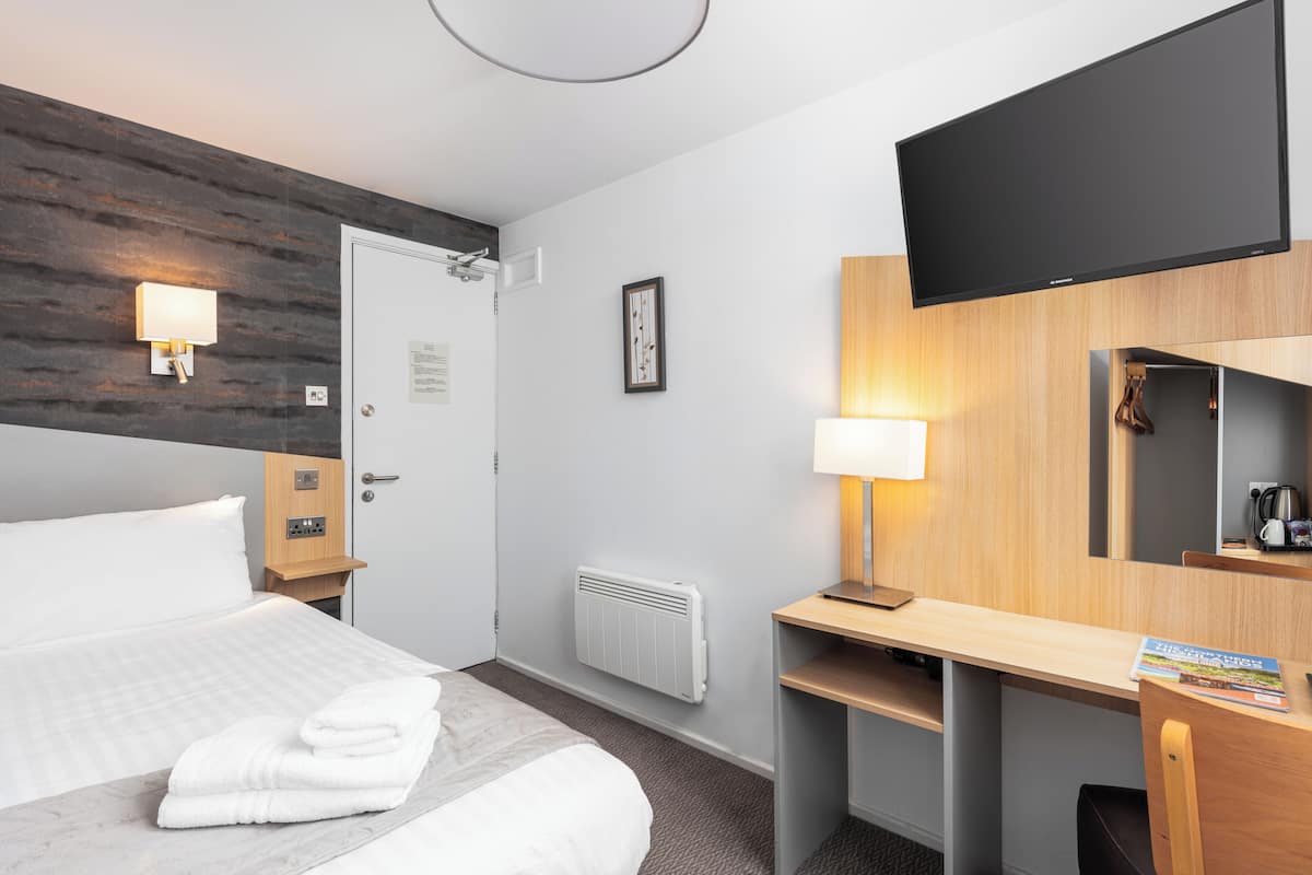 A hotel room with a bed, a desk, a TV, a lamp, and a radiator.