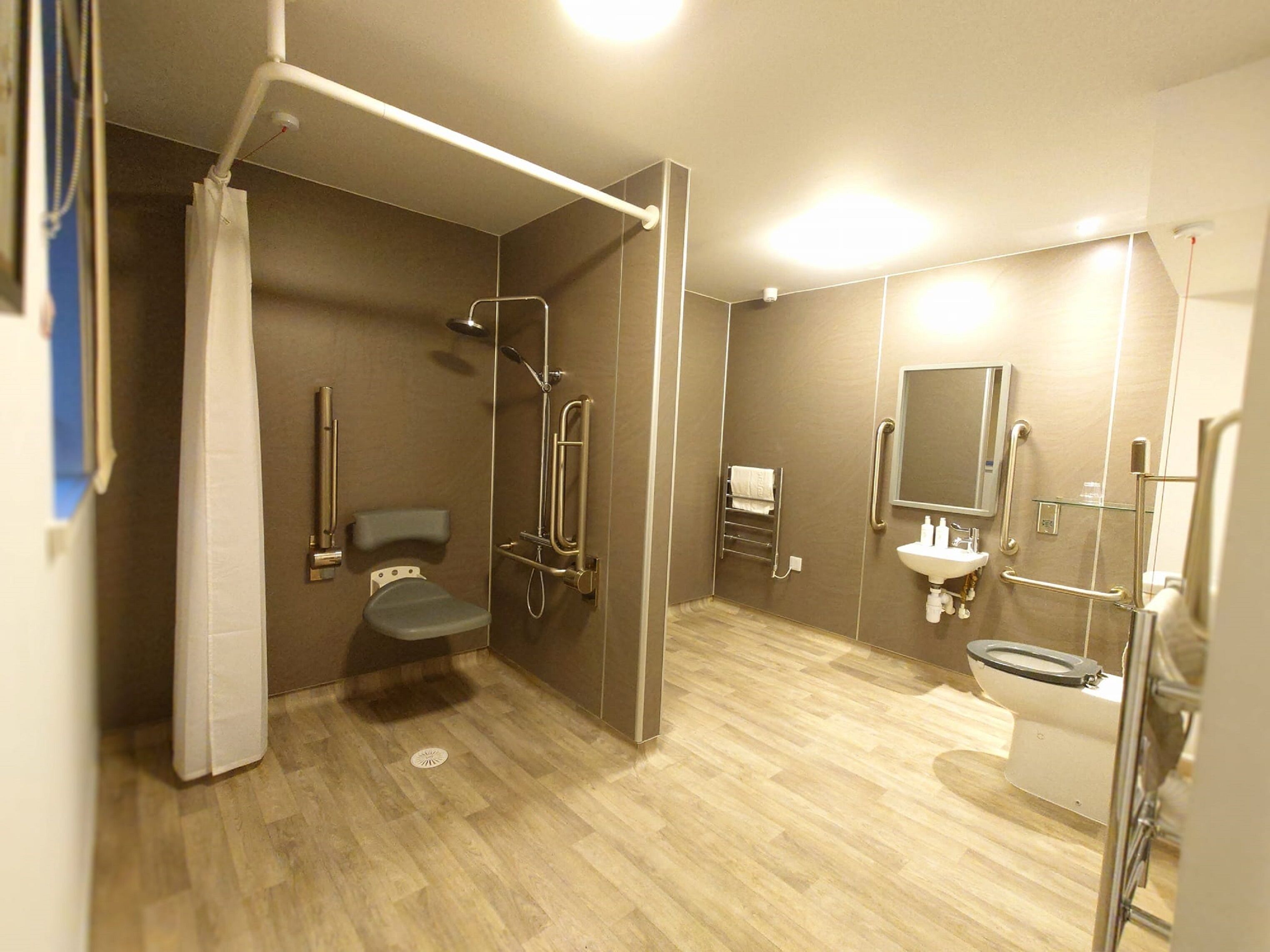 A modern bathroom with a shower, toilet, and sink, equipped with grab bars and a handrail.