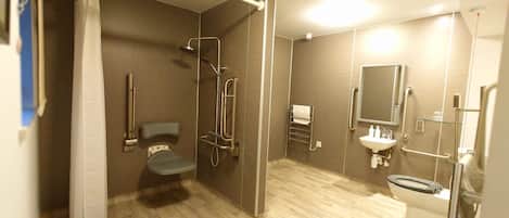 A modern bathroom with a shower, toilet, and sink, equipped with grab bars and a handrail.