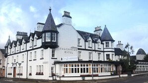 A traditional Caledonian Hotel with multiple chimneys, a prominent sign, and a corner location with a street view. - Caledonian Hotel (Ullapool)