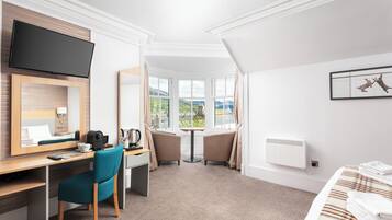 A hotel room with a desk, chair, bed, TV, window, and artwork.