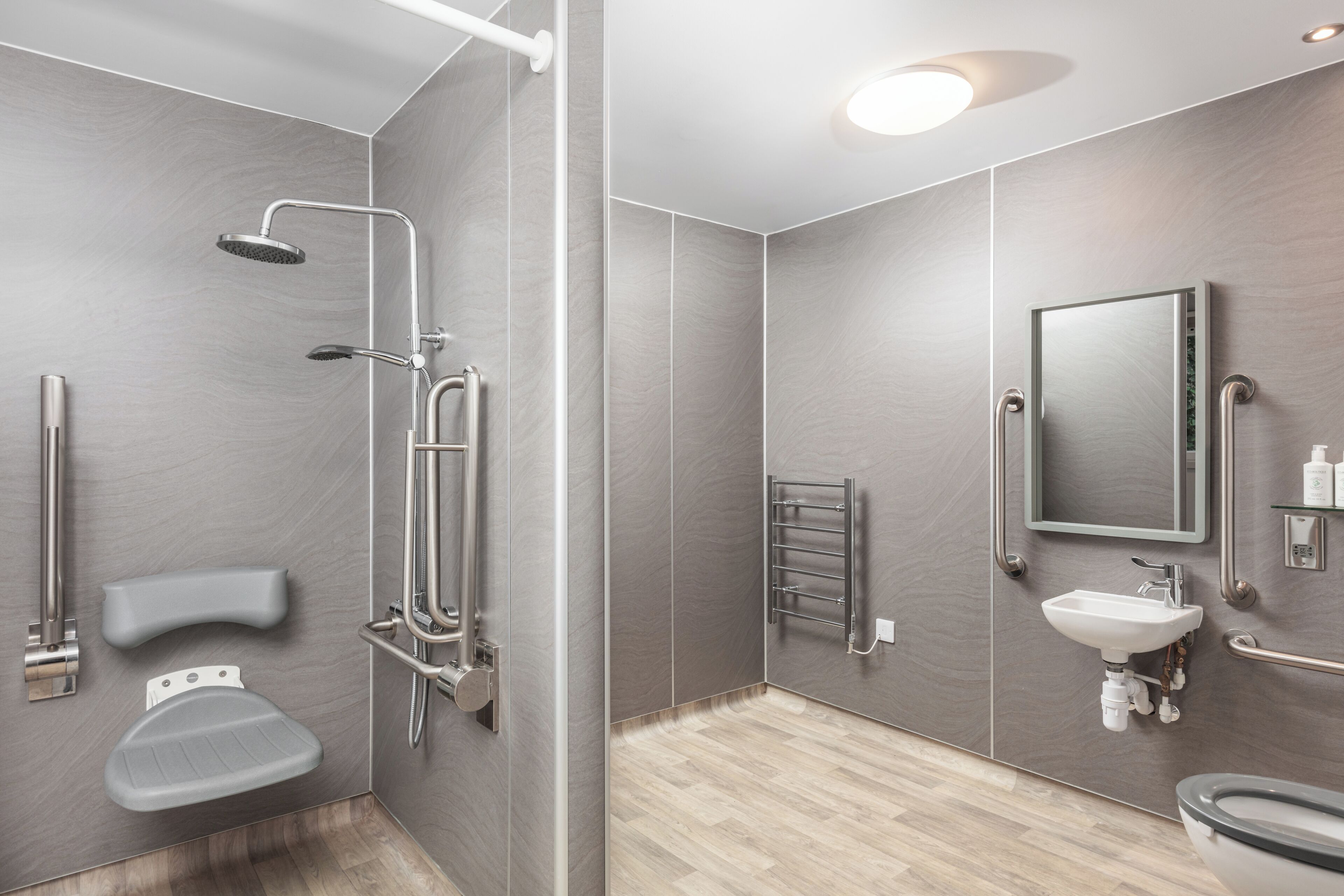 Ein modernes Badezimmer mit Dusche, Toilette und Waschbecken, ausgestattet mit Haltegriffen und einer Handstange.