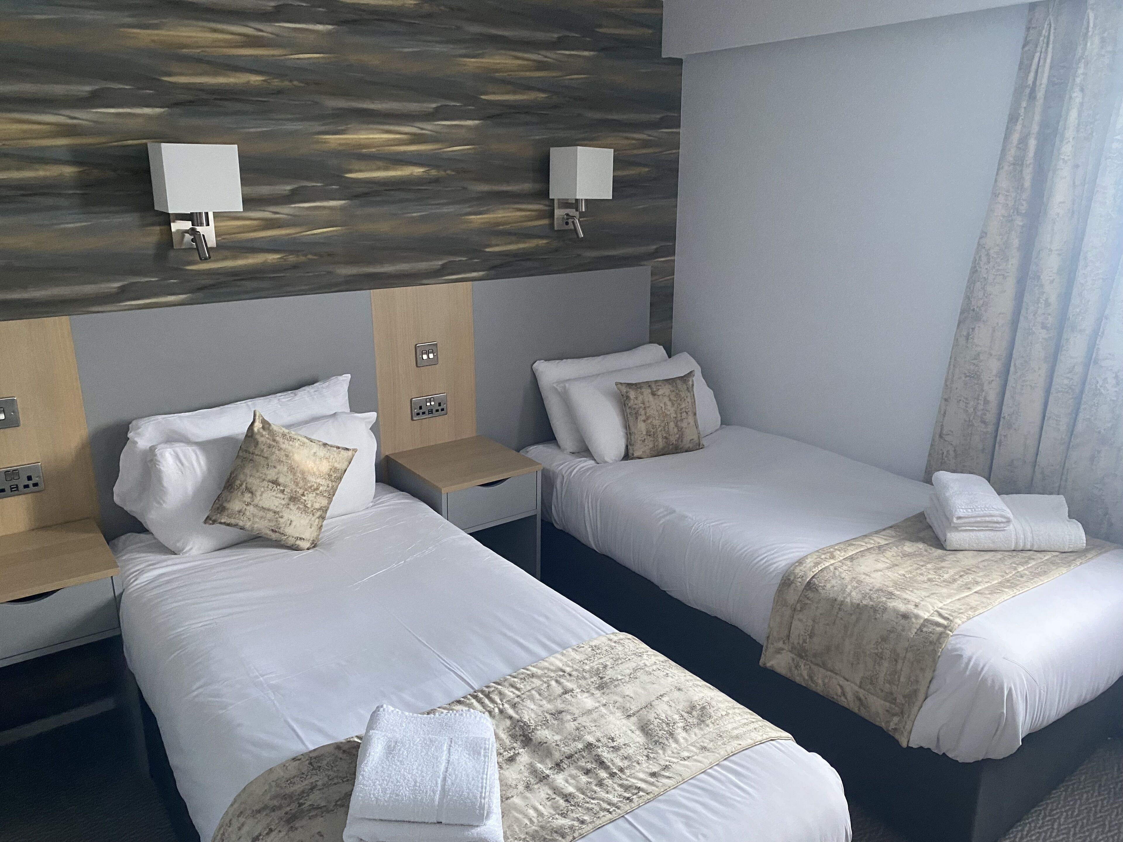 Ein Hotelzimmer mit zwei Betten, jeweils mit Kissen, einem Nachttisch und einer Lampe.