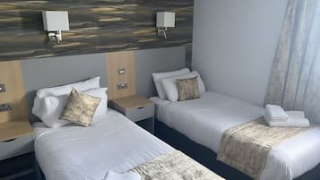Une chambre d’hôtel avec deux lits, chacun étant équipé d’un oreiller, d’une table de chevet et d’une lampe.
