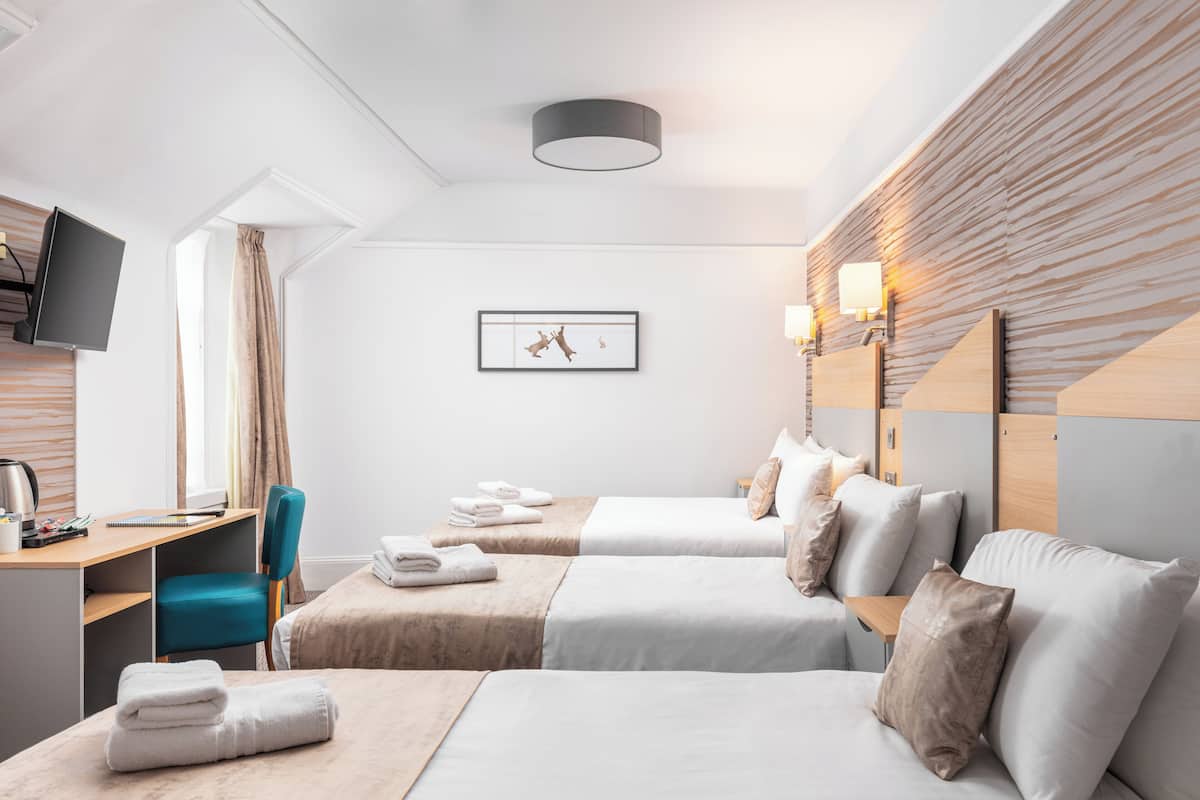 A hotel room with two beds, a desk, a chair, and a television.