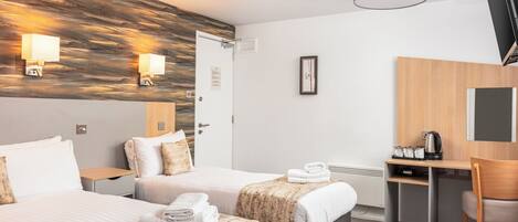 Habitación de hotel con dos camas, un escritorio, una silla, un televisor de pantalla plana y una lámpara de pared.