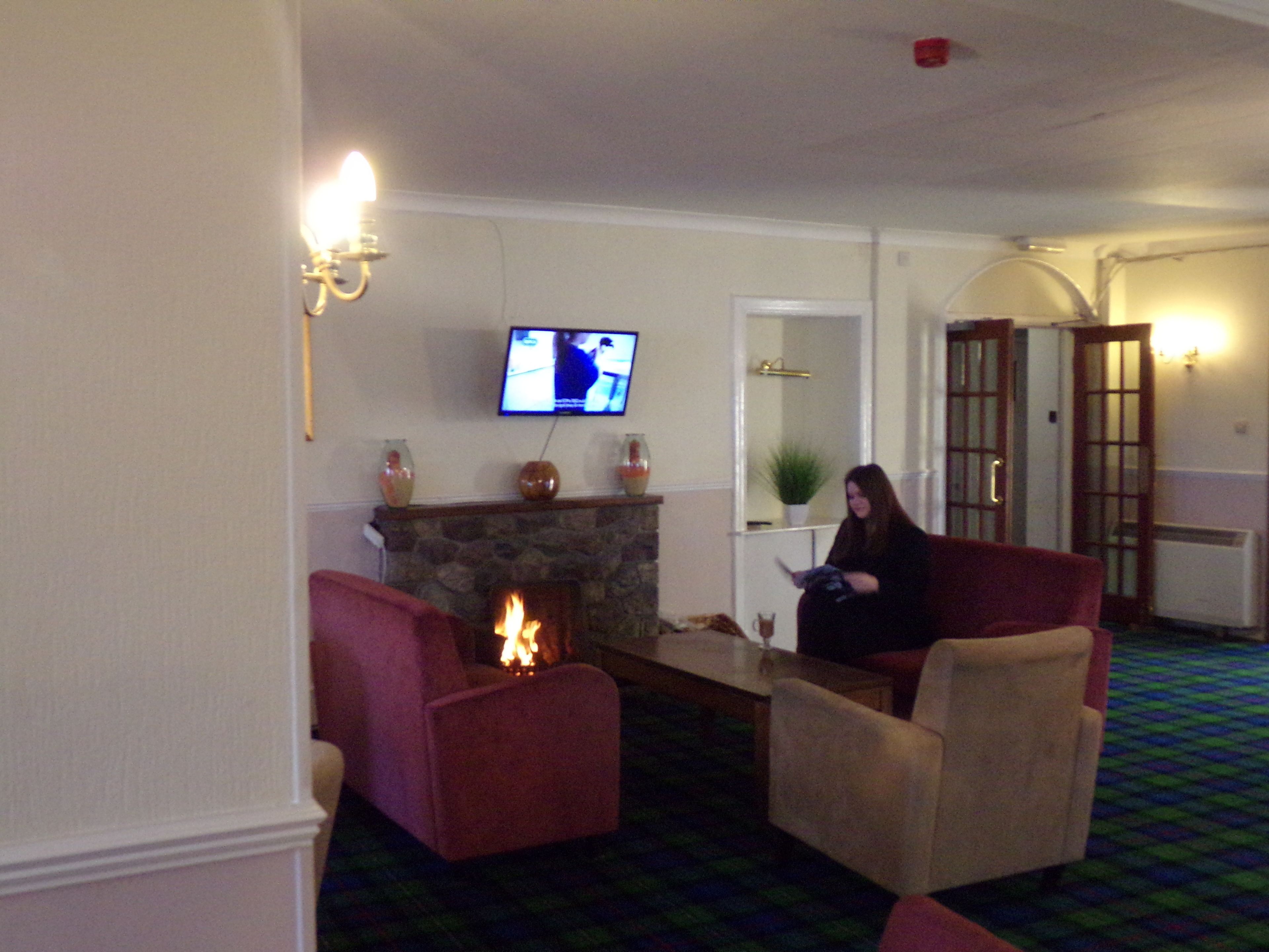 A living room with a fireplace, a television mounted on the wall, and a person sitting on a chair.