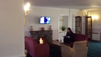 A living room with a fireplace, a television mounted on the wall, and a person sitting on a chair.