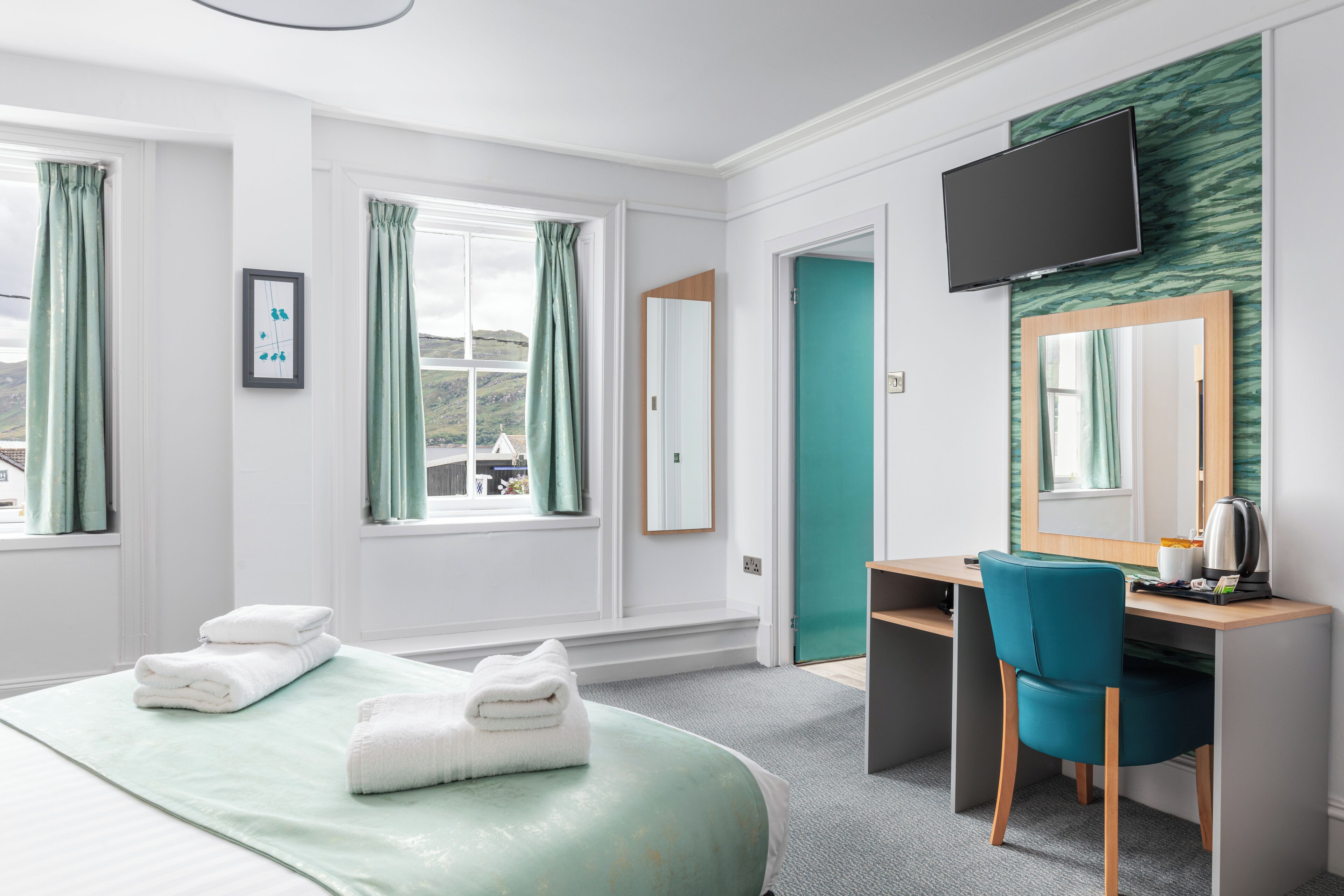 A hotel room with a bed, a desk, a chair, a television, and a view of the outside.
