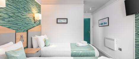 Quarto de hotel com duas camas, televisão presa à parede, tomada elétrica e uma porta.