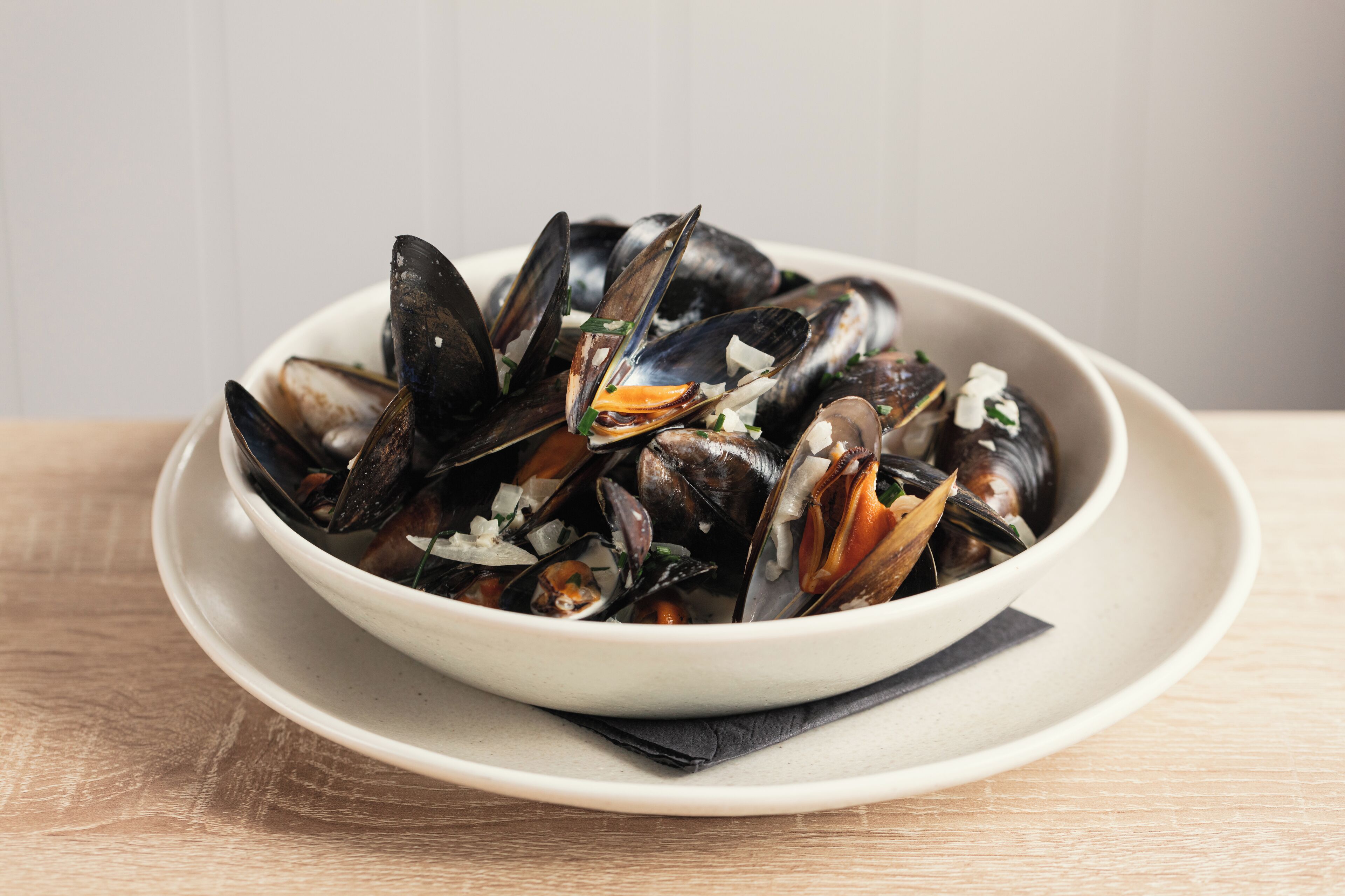 A bowl of mussels on a white plate.