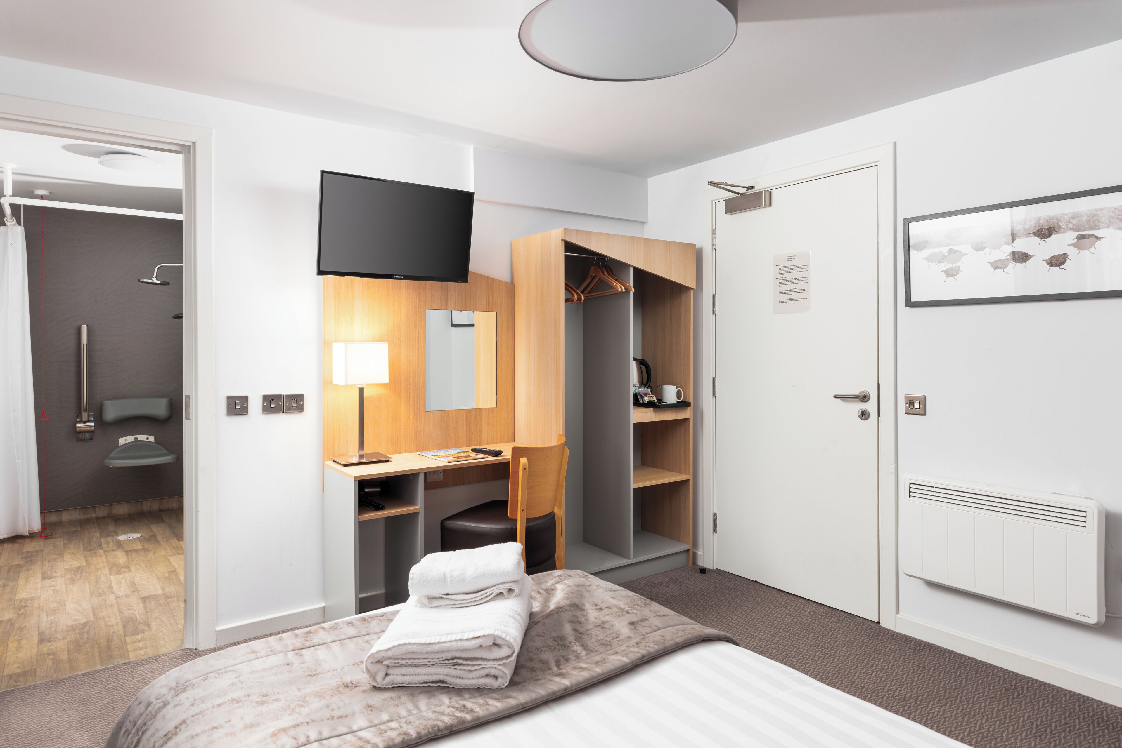 Habitació d'hotel moderna amb llit, escriptori, armari i zona de banyera amb dutxa.