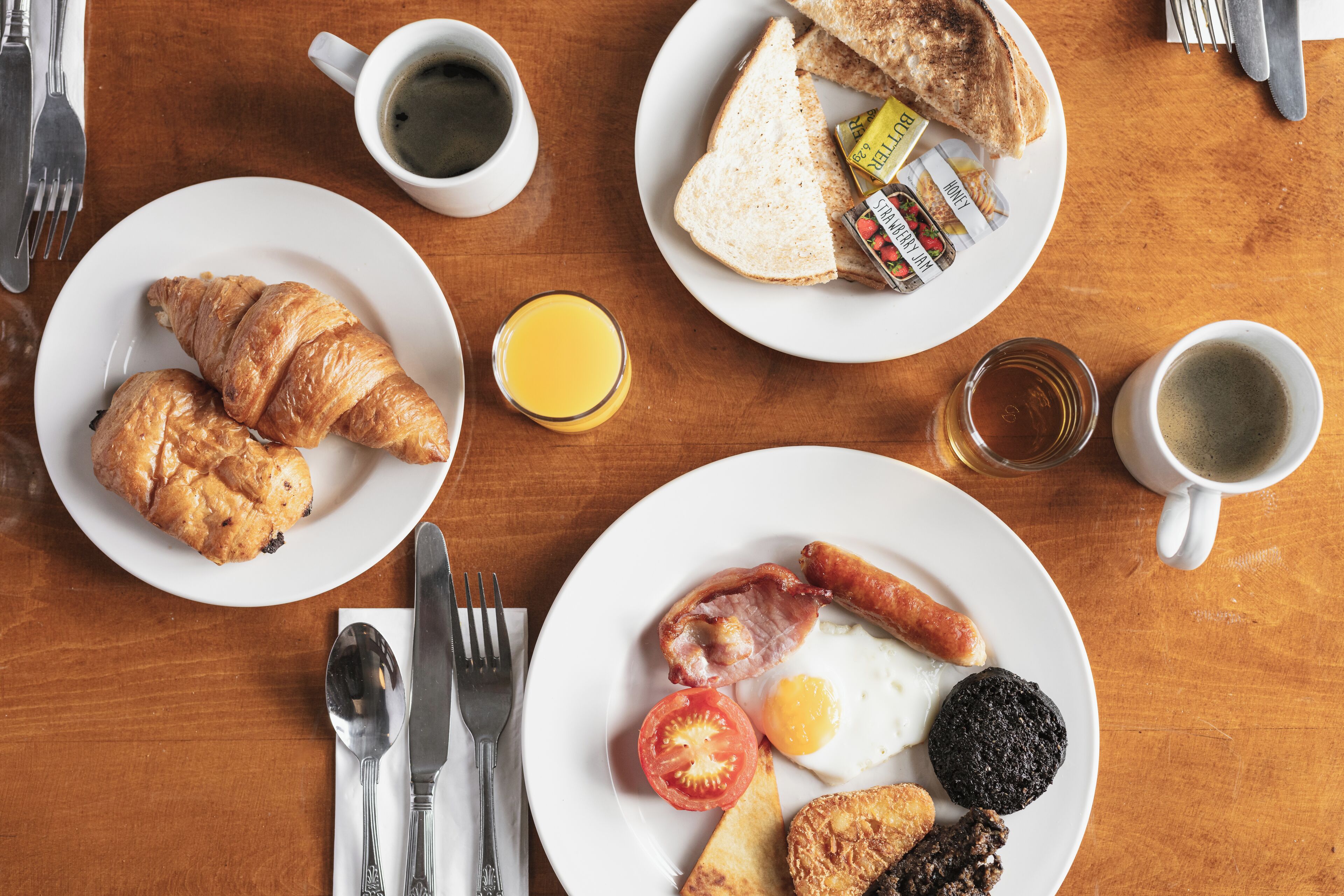 A breakfast table with croissants, toast, sausages, eggs, tomatoes, and juice.