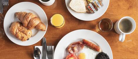 A breakfast table with croissants, toast, sausages, eggs, tomatoes, and juice.