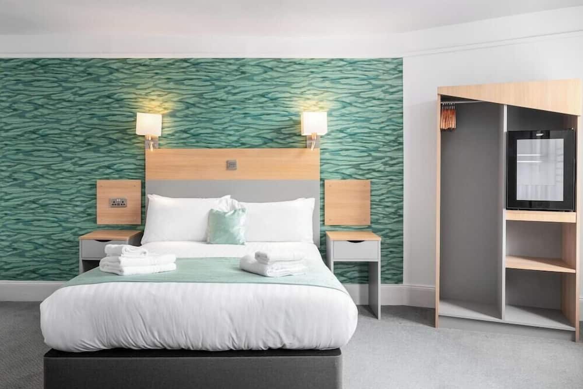 A hotel room with a bed, two bedside lamps, a wardrobe, and a green textured wall.