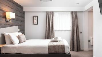 Een moderne hotelkamer met een groot bed, een nachtkastje, een wandlamp, een lijst met een afbeelding en een raam met gordijnen.