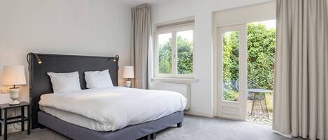 A modern bedroom with a large bed, bedside lamps, and a view of the outdoors through a sliding glass door.