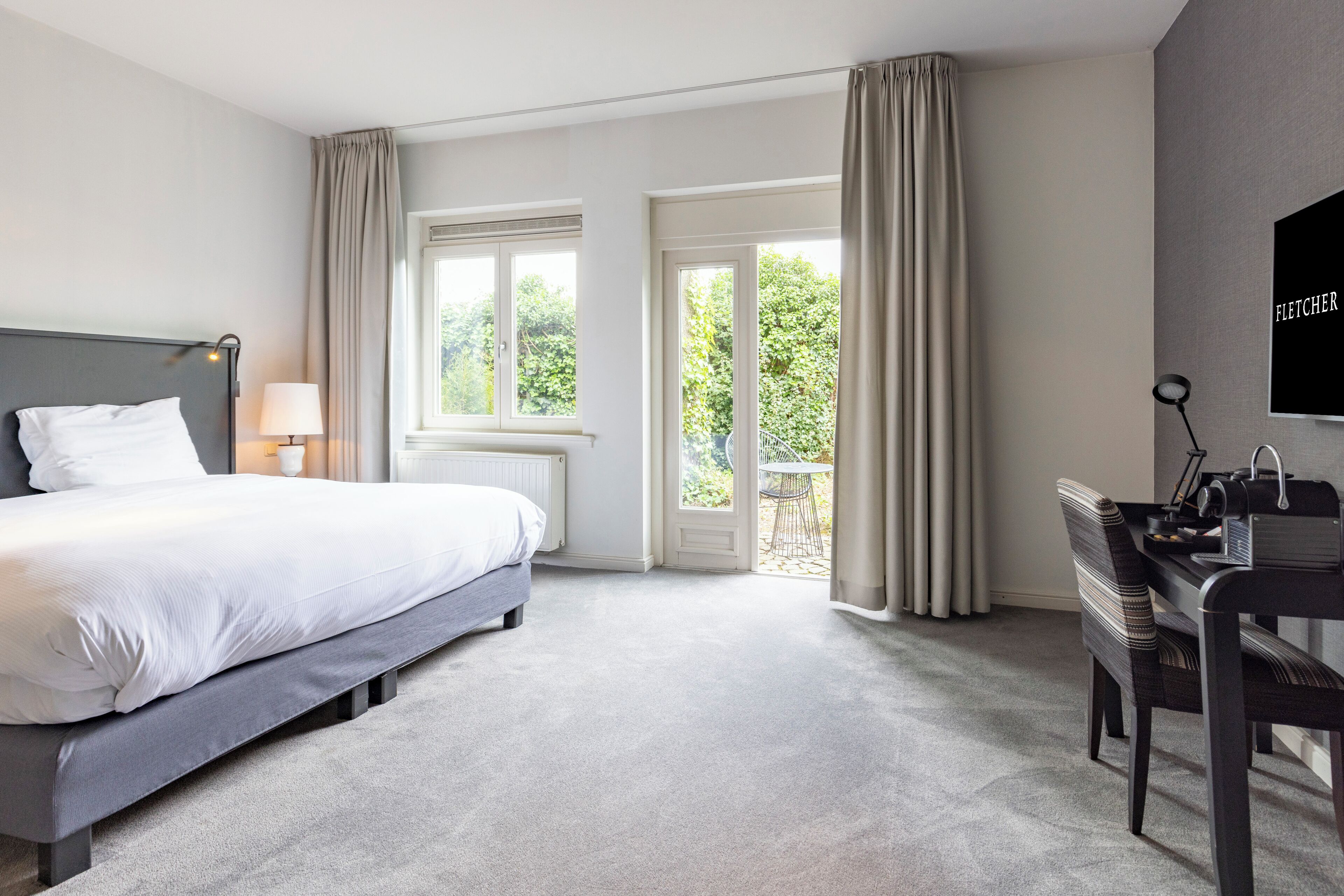 Une chambre d’hôtel avec un lit, un bureau, une chaise, une télévision et un balcon avec des rideaux.