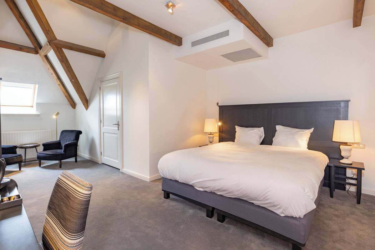A bedroom with a large bed, two bedside tables with lamps, a chair, and a small table.