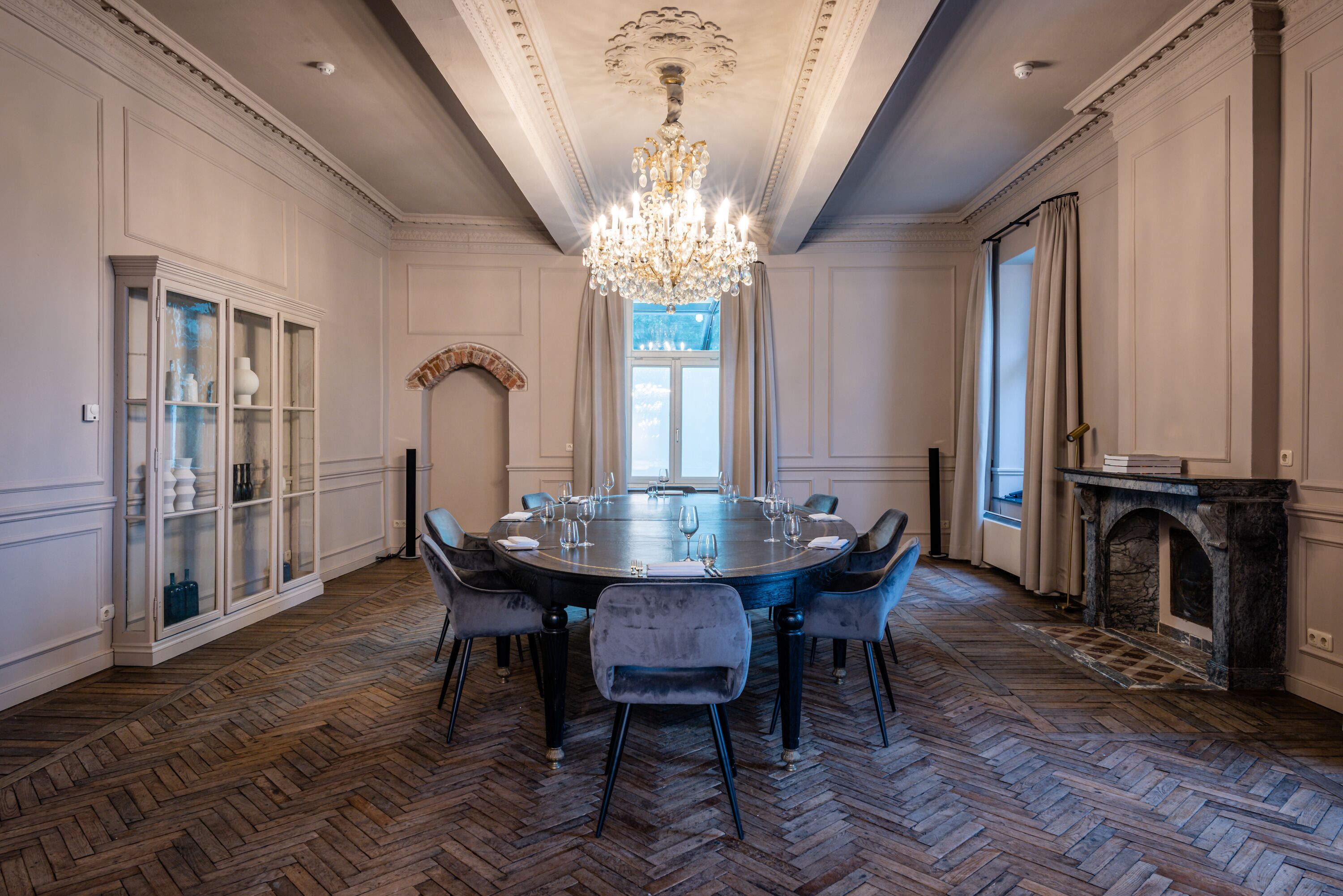 Een formele eetzaal met een ronde tafel, stoelen, een kroonluchter en een open haard.
