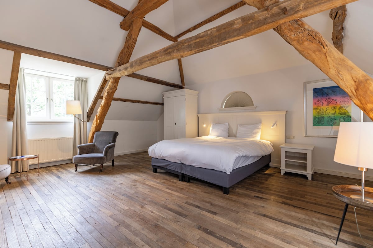 A bedroom with a wooden ceiling, a bed, a chair, a nightstand, and a lamp.