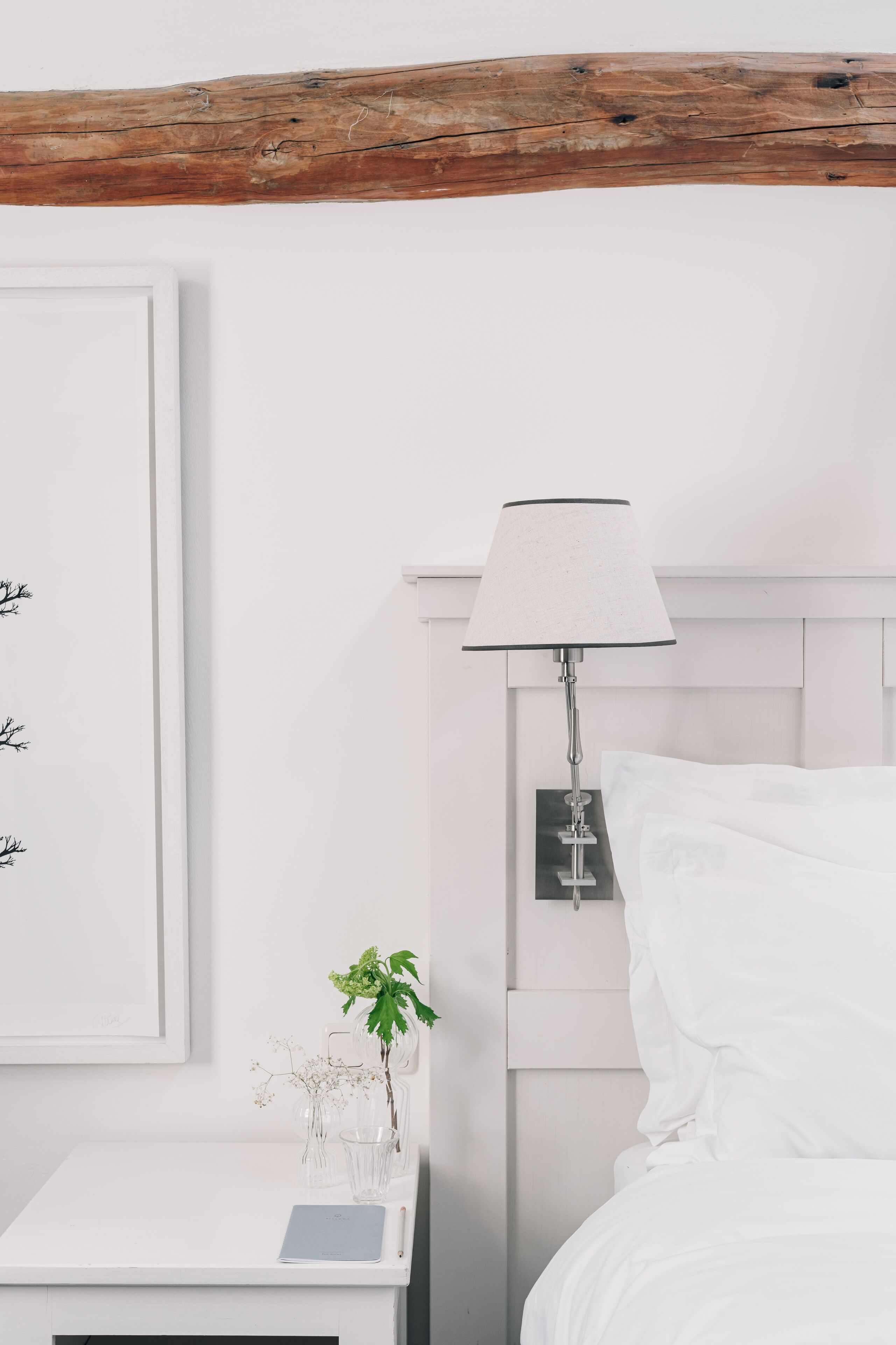 Un dormitorio ordenado con una cama blanca, una mesita de noche con lámpara y un cuadro enmarcado en la pared.