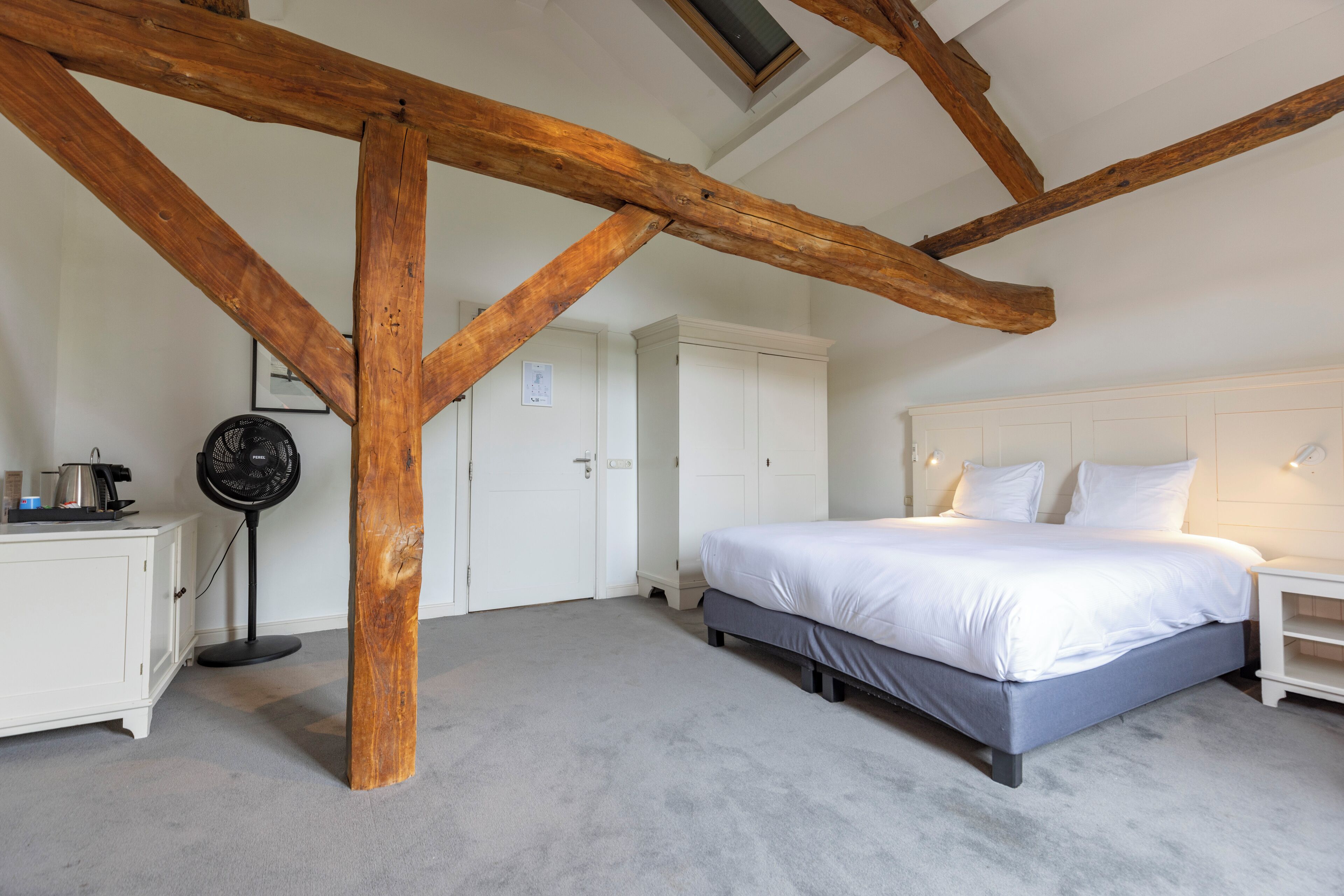 Un dormitorio con una cama grande, vigas de madera, un armario blanco y un ventilador.